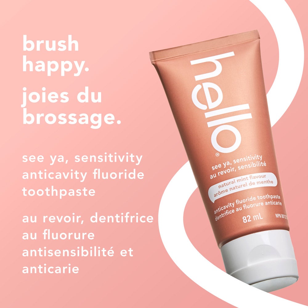 A tube of hello See Ya Sensitivity toothpaste, natural mint flavor, displayed at an angle on a light pink and white curved background. Text above and beside the tube reads &quot;brush happy&quot; and &quot;see ya, sensitivity anticavity fluoride toothpaste&quot; in both English and French.