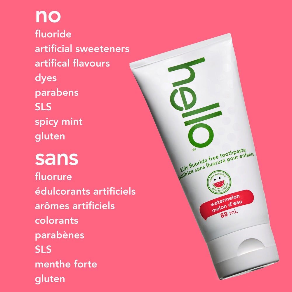 A tube of hello kids watermelon fluoride free toothpaste is angled on a solid pink background. The text beside it lists what the product does not contain: &quot;no fluoride, artificial sweeteners, artificial flavours, dyes, parabens, SLS, spicy mint, gluten.&quot;