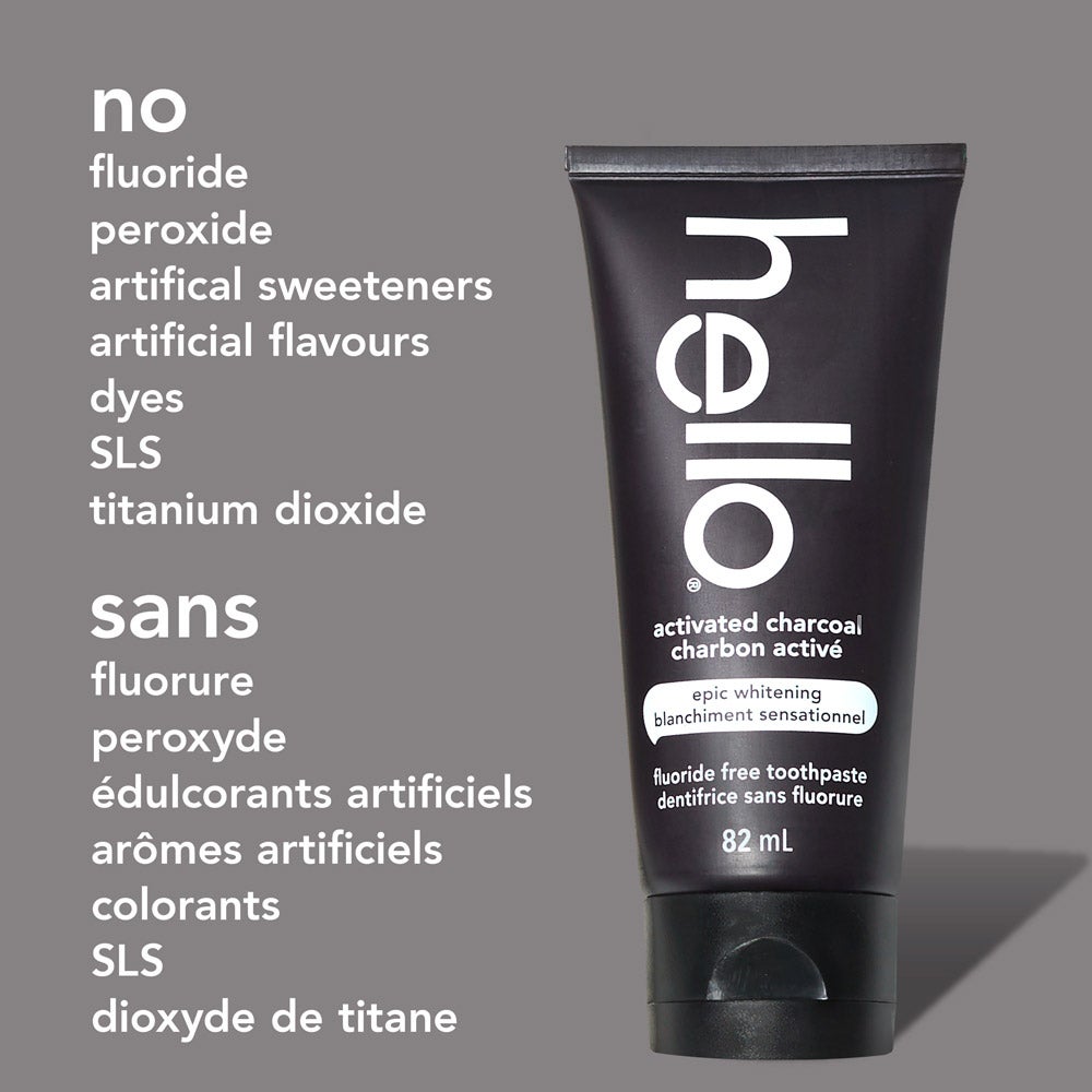 A tube of hello epic whitening charcoal fluoride free toothpaste stands upright against a light gray background. To the left of the tube, text lists: &quot;no fluoride, peroxide, artificial sweeteners, artificial flavours, dyes, SLS, titanium dioxide&quot; in English and the same in French below.