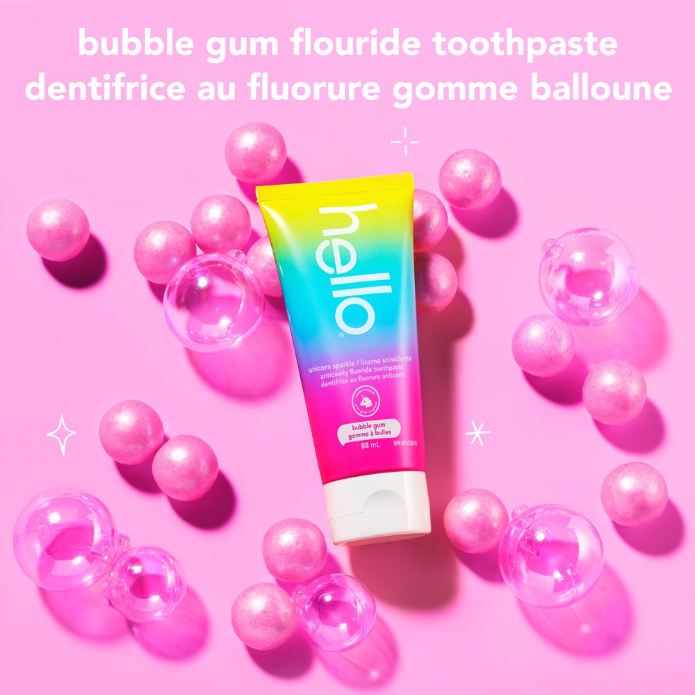 A tube of hello unicorn sparkle bubble gum fluoride toothpaste is placed among scattered pink bubble gum balls and clear bubbles on a light pink background. The text above reads, &quot;bubble gum fluoride toothpaste.&quot;