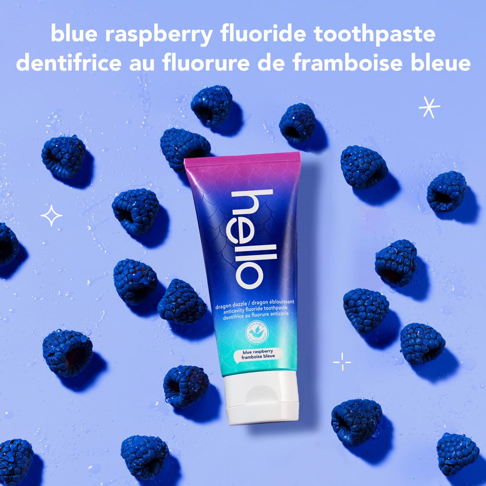 A tube of hello dragon dazzle blue raspberry fluoride toothpaste is surrounded by several fresh blue raspberries on a light blue background. The text reads, &quot;blue raspberry fluoride toothpaste.&quot;