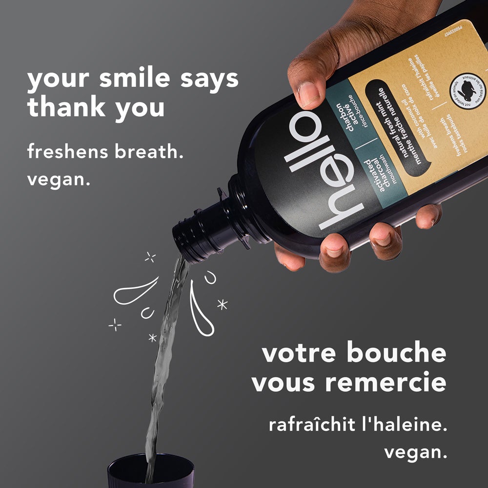 A close-up of a hand pouring hello brand activated charcoal mouthwash into a cup against a gray background. White text says &quot;your smile says thank you – freshens breath. vegan.&quot; in English and the French translation below. The product bottle label is visible.